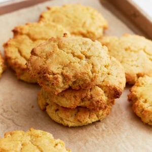 Freshly baked almond flour biscuits stacked on a parchment-lined baking sheet, golden and crumbly with slightly crisp edges.