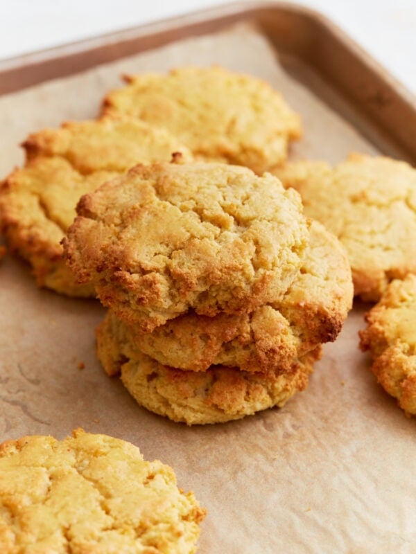 Freshly baked almond flour biscuits stacked on a parchment-lined baking sheet, golden and crumbly with slightly crisp edges.