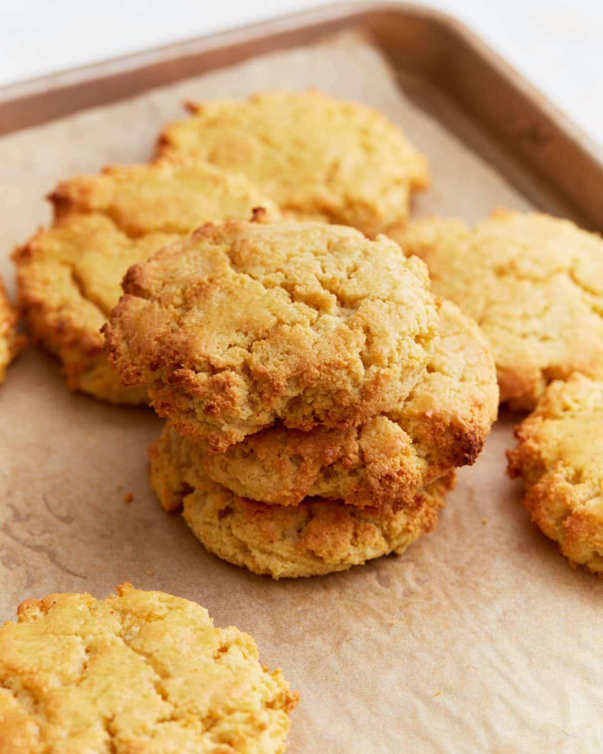Freshly baked almond flour biscuits stacked on a parchment-lined baking sheet, golden and crumbly with slightly crisp edges.