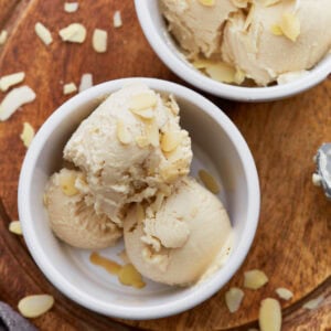 Close-up of creamy almond milk ice cream scooped into a white ramekin, topped with sliced almonds, sitting on a wooden board.