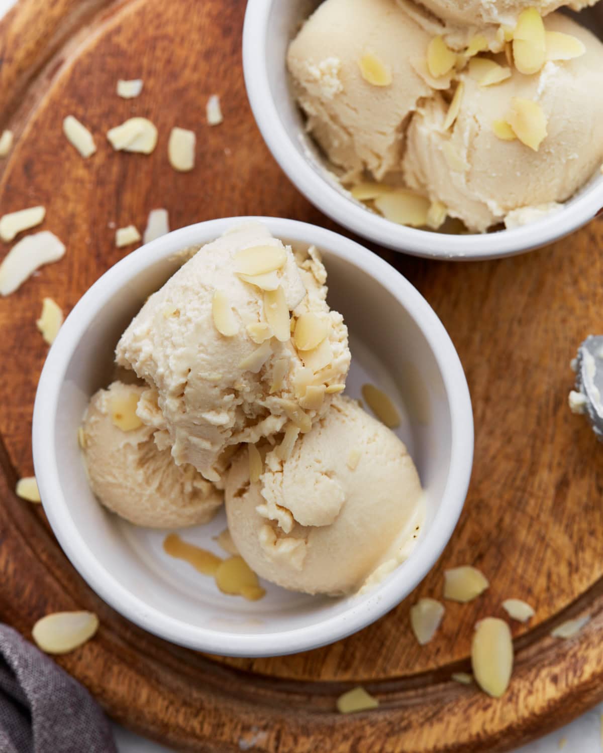 Close-up of creamy almond milk ice cream scooped into a white ramekin, topped with sliced almonds, sitting on a wooden board.