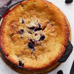 Overhead view of a golden-brown gluten-free blackberry cobbler freshly baked in a round black dish, with blackberries peeking through the crust.