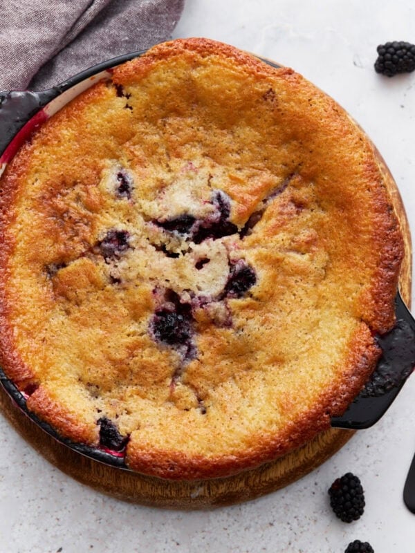 Overhead view of a golden-brown gluten-free blackberry cobbler freshly baked in a round black dish, with blackberries peeking through the crust.