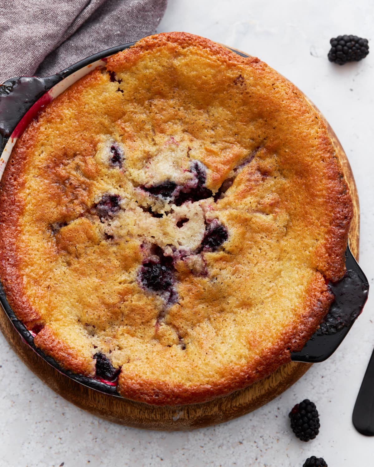 Overhead view of a golden-brown gluten-free blackberry cobbler freshly baked in a round black dish, with blackberries peeking through the crust.