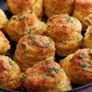 Freshly baked gluten-free cheddar bay biscuits in a cast iron skillet, topped with melted garlic butter and chopped parsley.