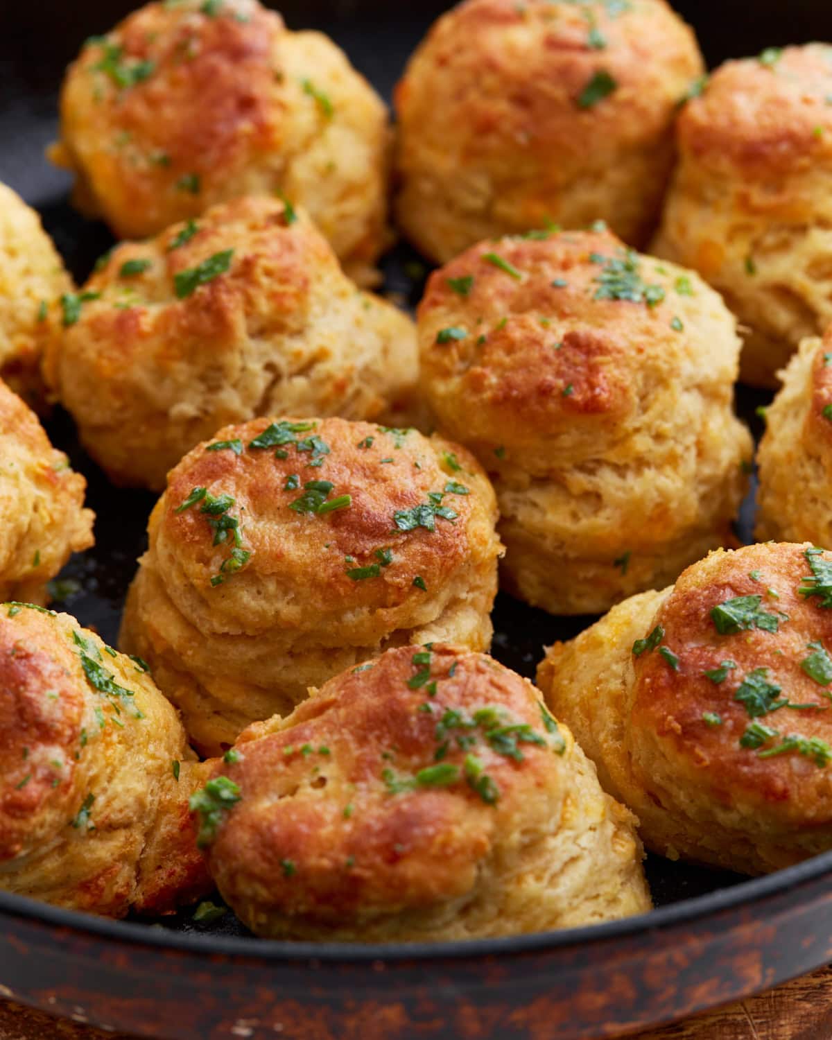 Freshly baked gluten-free cheddar bay biscuits in a cast iron skillet, topped with melted garlic butter and chopped parsley.