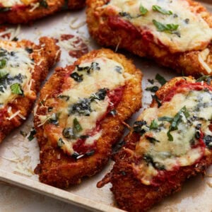 Crispy, golden-brown gluten-free chicken parmesan topped with melted cheese, marinara sauce, and fresh basil on a baking sheet.