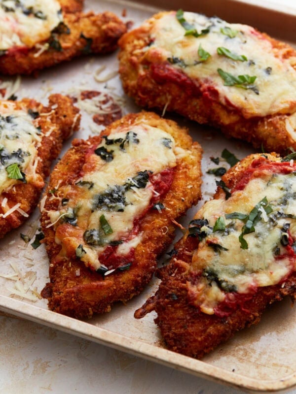 Crispy, golden-brown gluten-free chicken parmesan topped with melted cheese, marinara sauce, and fresh basil on a baking sheet.