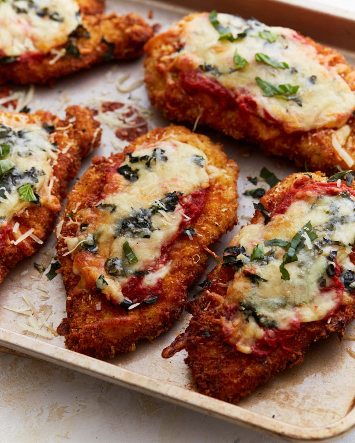 Crispy, golden-brown gluten-free chicken parmesan topped with melted cheese, marinara sauce, and fresh basil on a baking sheet.