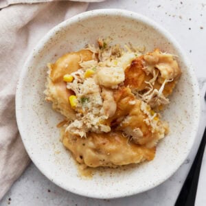 A serving of gluten-free chicken and dumplings casserole on a white speckled plate with visible chunks of biscuit topping, shredded chicken, corn, and creamy sauce.