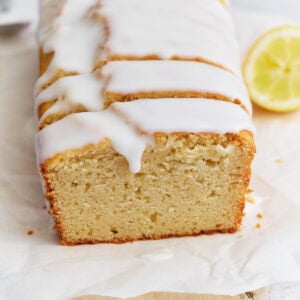 Sliced gluten-free iced lemon loaf on parchment paper with a thick white glaze dripping over the edges.