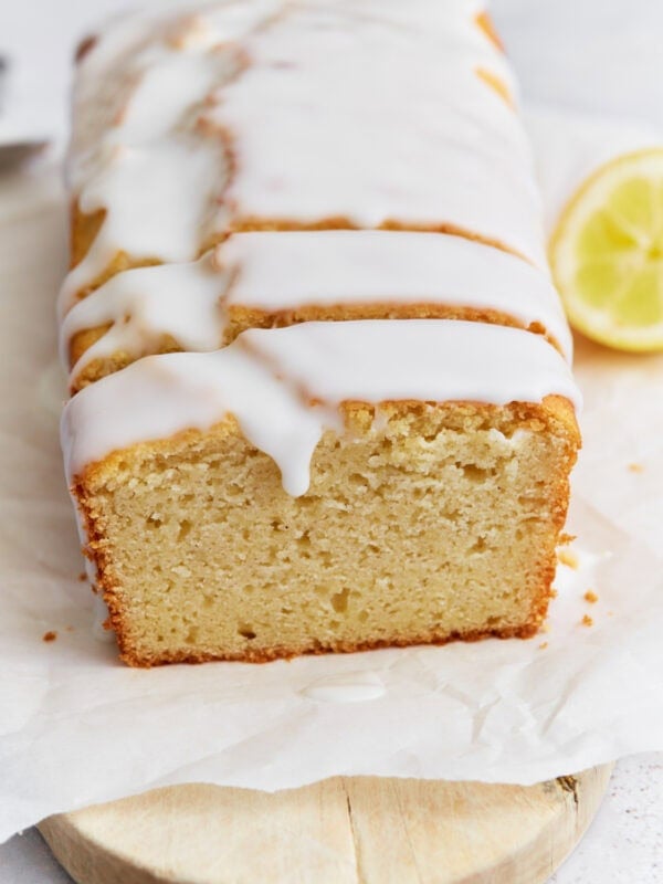 Sliced gluten-free iced lemon loaf on parchment paper with a thick white glaze dripping over the edges.
