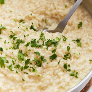 Creamy gluten-free risotto in a pan topped with chopped fresh parsley, with a serving spoon scooping from the center.