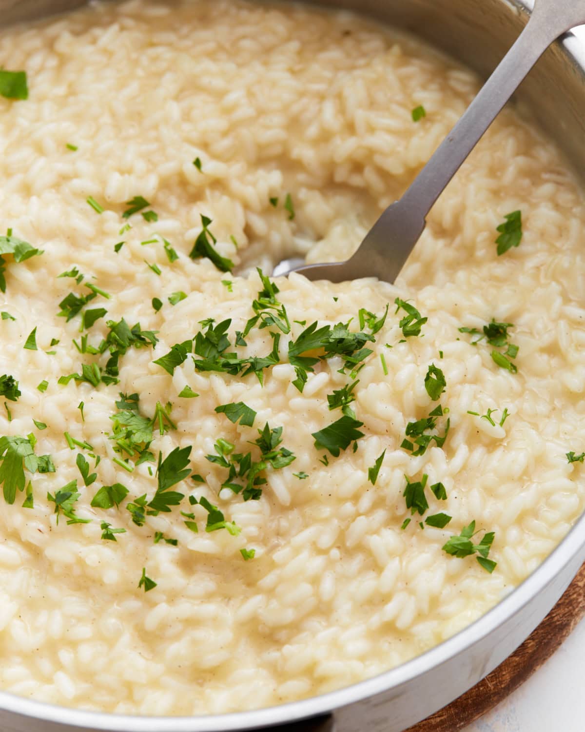 Creamy gluten-free risotto in a pan topped with chopped fresh parsley, with a serving spoon scooping from the center.