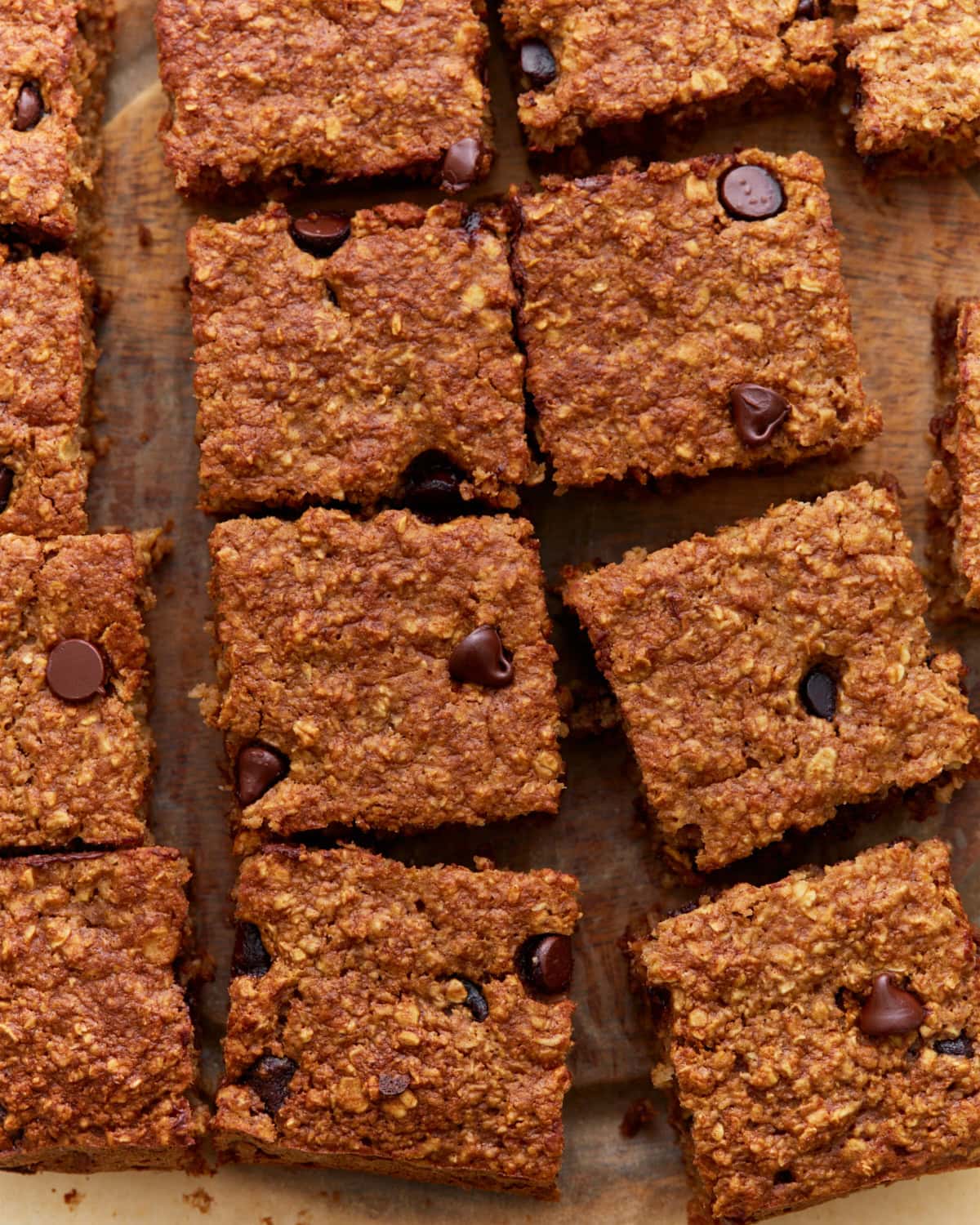 Close-up of sliced baked oatmeal bars with chocolate chips on a wooden surface, showing a golden-brown, chewy texture.