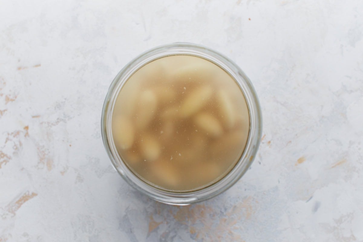 Top-down view of a glass jar filled with soaked blanched almonds in water.