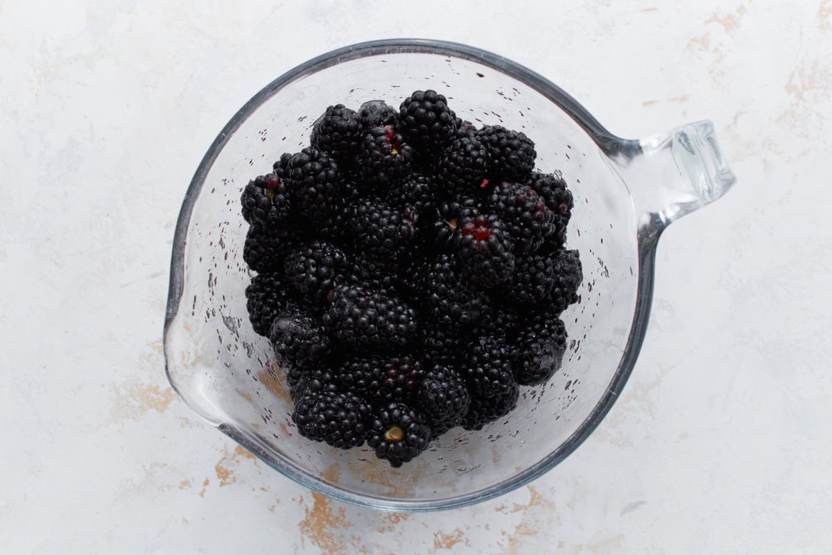 Glass measuring cup filled with fresh blackberries on a light background.