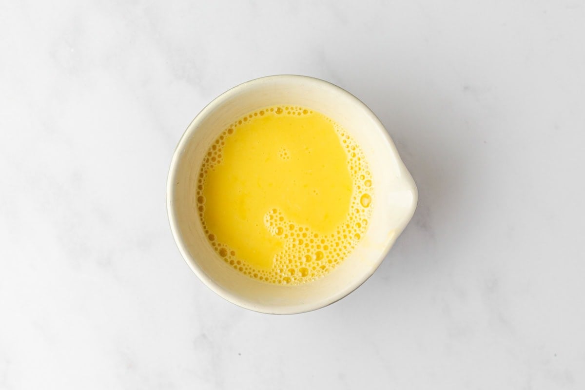 Small bowl of whisked egg and water mixture for egg wash on a white marble surface.