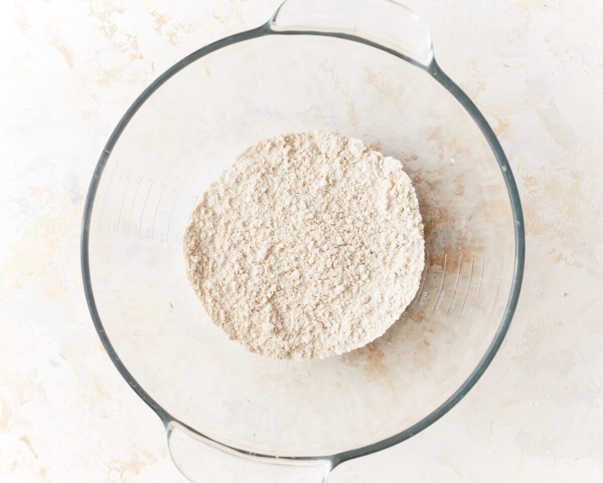A glass mixing bowl filled with gluten-free flour mixture, placed on a light countertop.