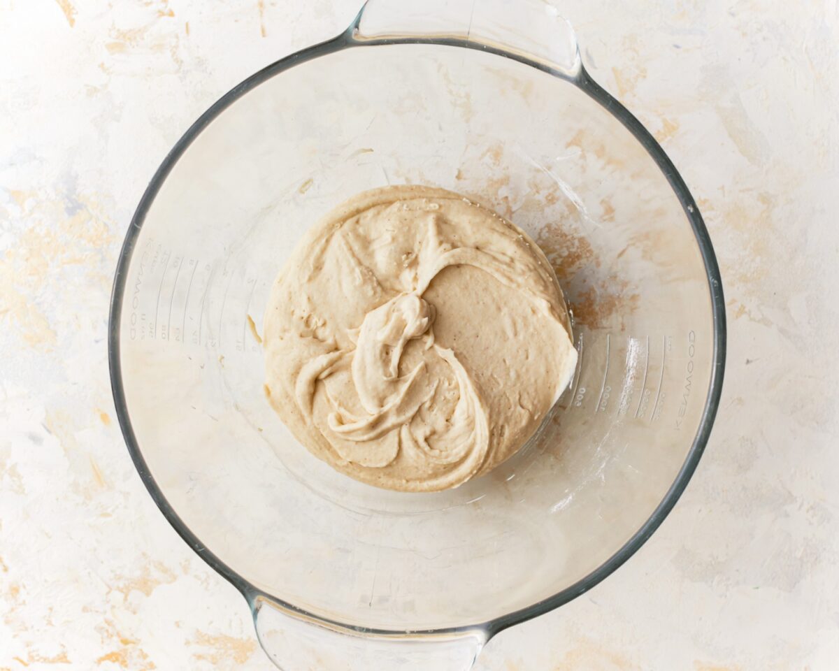 Gluten-free pizza dough just beginning to come together in a glass mixing bowl after mixing.