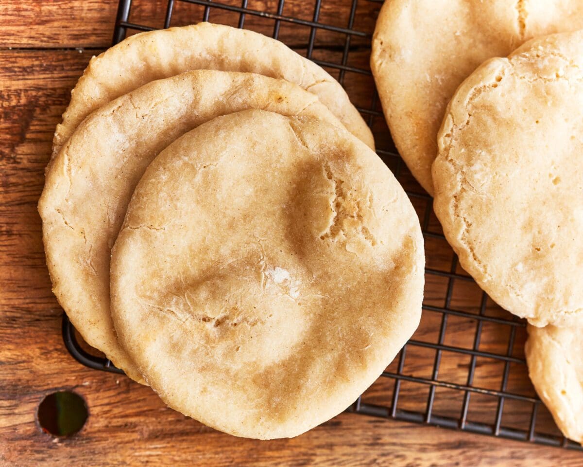 Baked gluten-free pitas resting on a wire rack, showing golden tops and light puffiness.