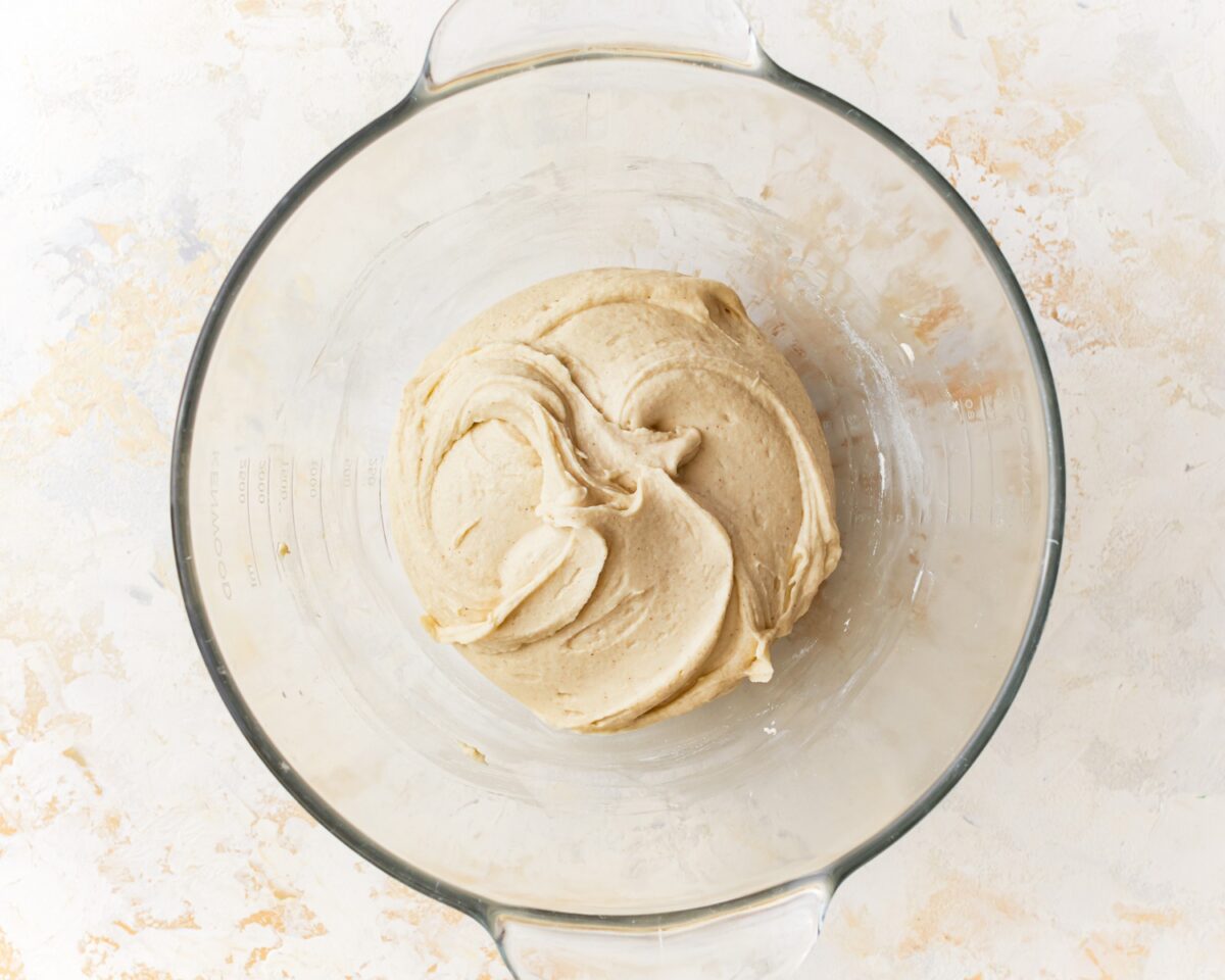 Gluten-free pizza dough fully mixed and slightly smoother in texture, resting in a glass mixing bowl.