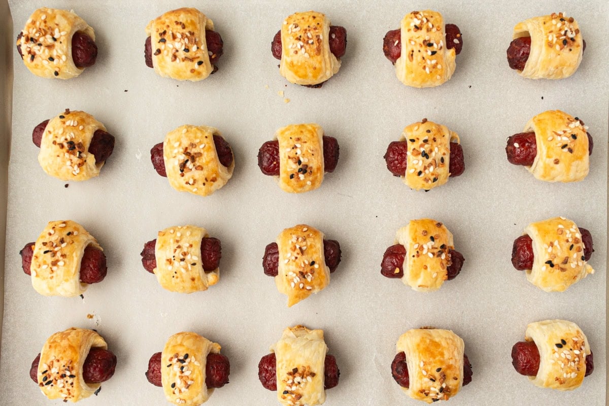Freshly baked gluten-free pigs in a blanket, golden and puffed, cooling on a parchment-lined baking sheet.