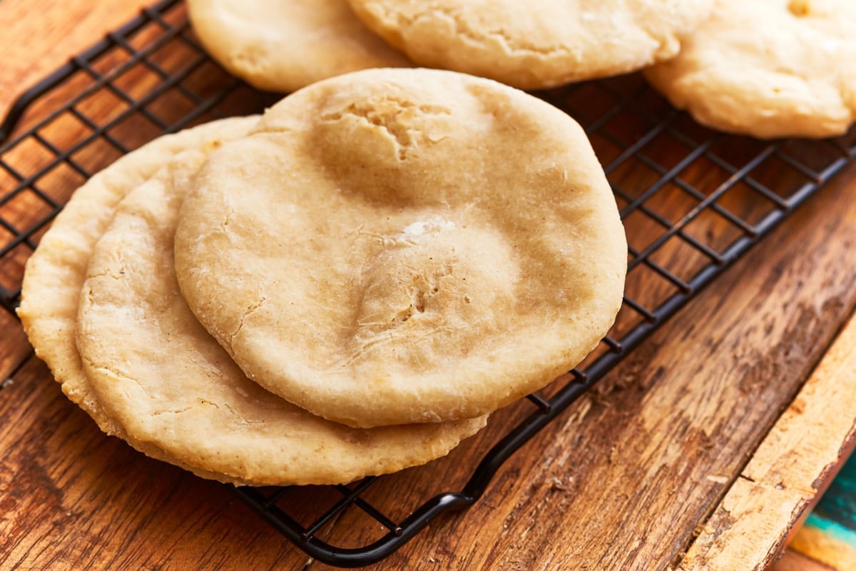 Angled view of a stack of gluten-free pita bread on a cooling rack over a rustic wooden table.