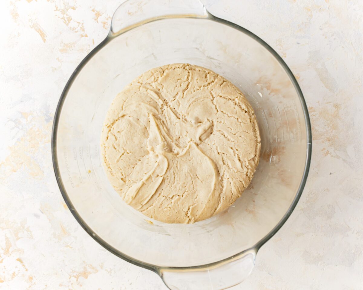 Gluten-free pizza dough after rising, showing a light and airy texture with visible cracks on the surface.