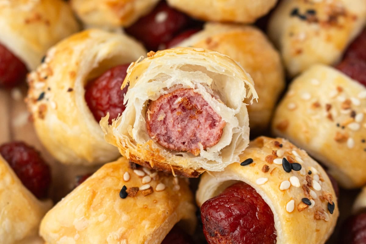 Close-up of a bitten pig in a blanket showing the flaky gluten-free puff pastry and juicy sausage center.