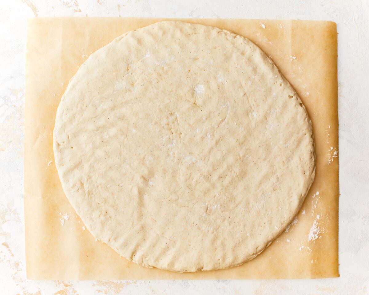Gluten-free pizza dough shaped into a 15-inch circle on floured parchment paper, ready to bake.