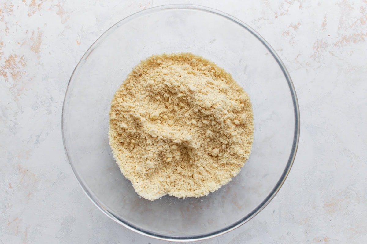 Dry ingredients in a glass bowl with chunks of butter just cut in, creating a coarse crumbly texture.