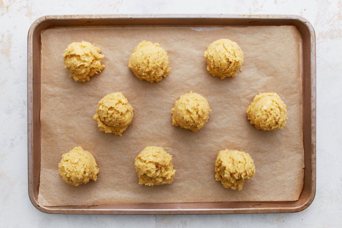 Nine scoops of almond flour biscuit dough spaced evenly on a parchment-lined baking sheet.