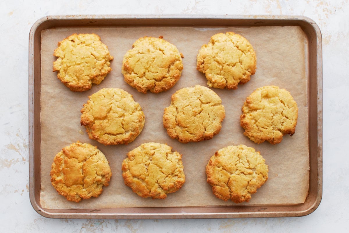 Freshly baked almond flour biscuits on a baking sheet, golden brown and slightly cracked on top.