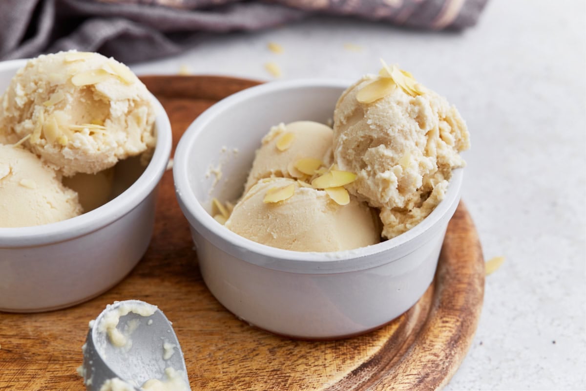 Side view of two bowls filled with almond milk ice cream, each topped with sliced almonds on a wood surface.