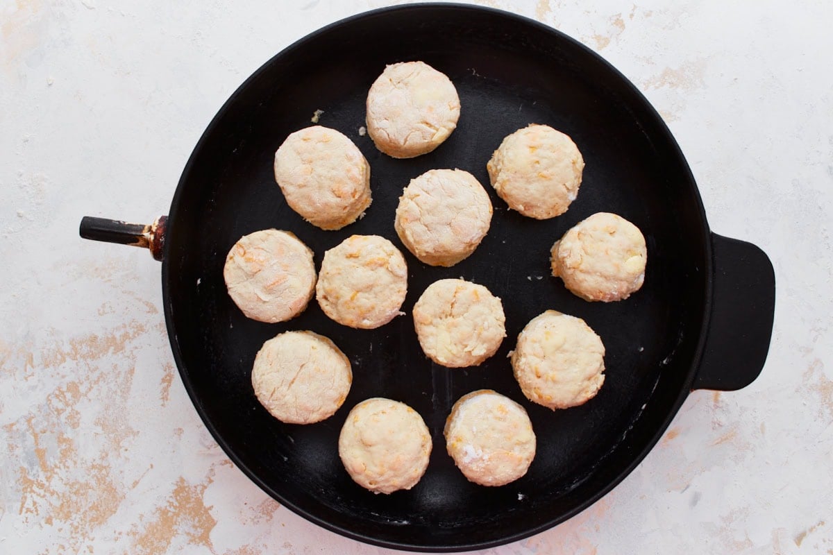 Raw biscuits evenly arranged in a cast iron skillet, ready to go into the freezer and then oven.