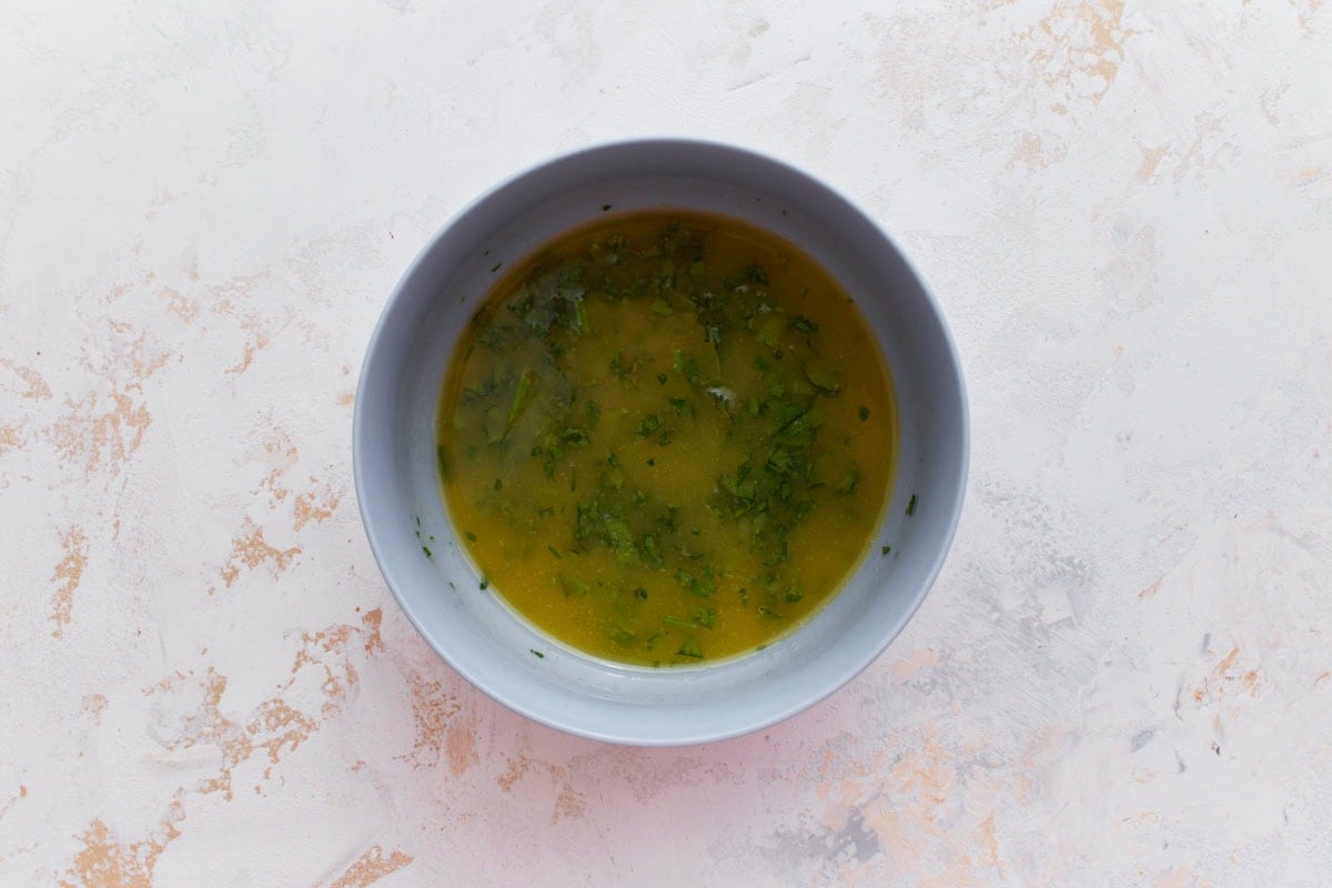 Small bowl of melted butter mixed with garlic powder, salt, and chopped fresh parsley.