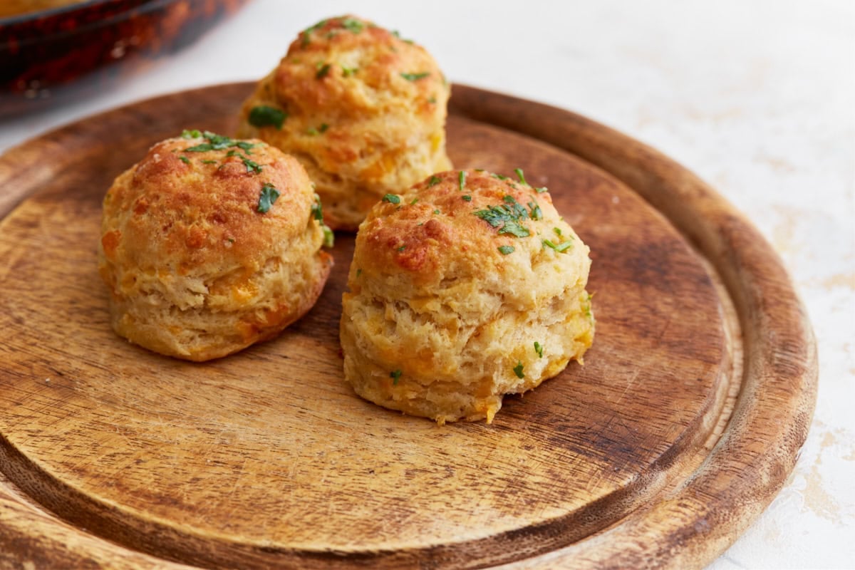 A few finished cheddar bay biscuits on a rustic wooden serving board, ready to enjoy.