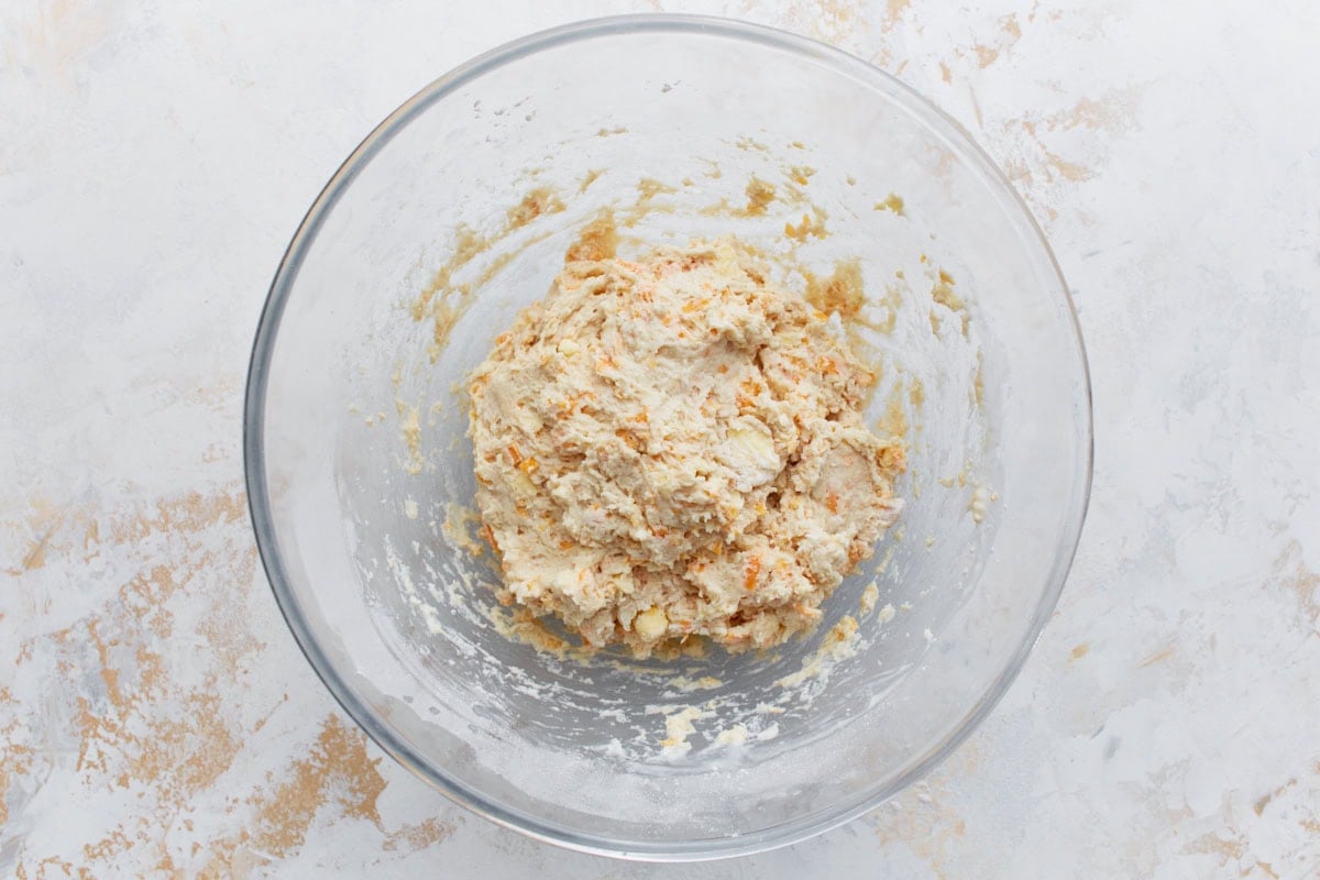 Sticky, textured biscuit dough with visible cheese shreds in a mixing bowl after stirring in buttermilk and egg.