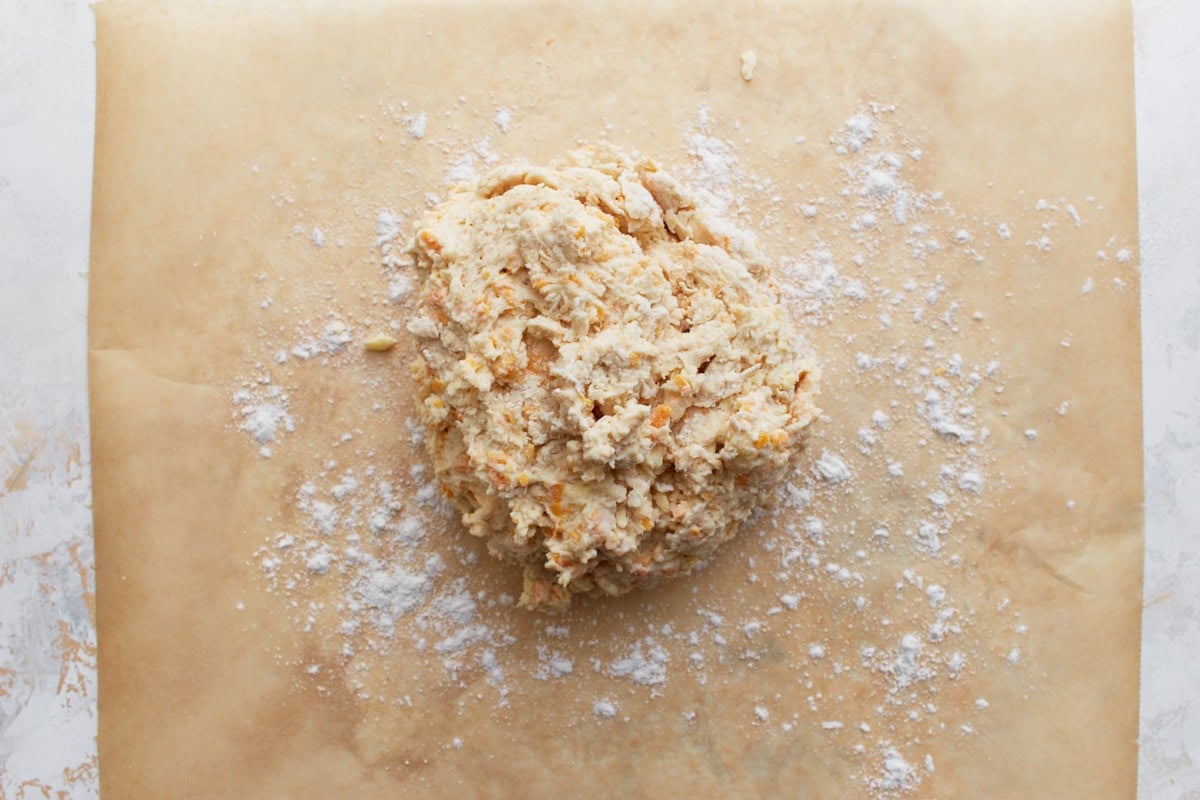 Mounded gluten-free dough placed on a floured sheet of parchment paper, ready to shape.