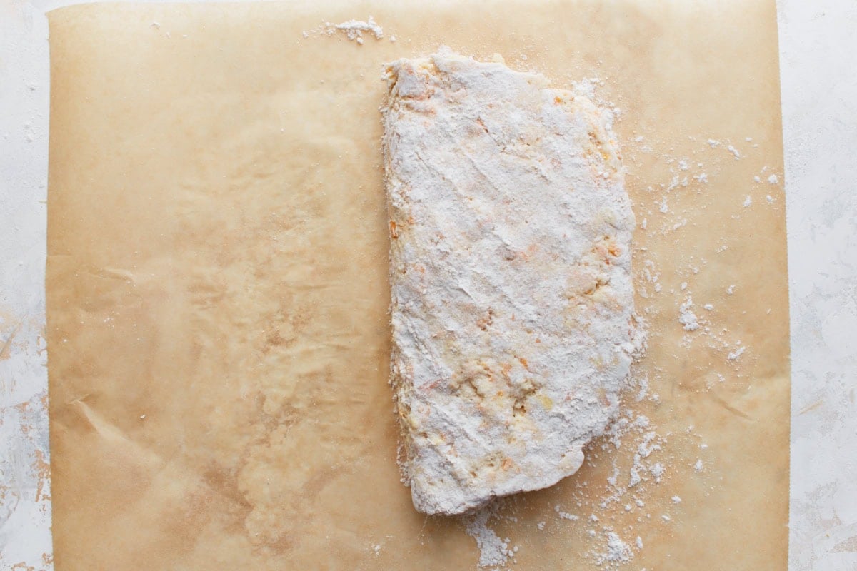 Biscuit dough folded in half to begin creating flaky layers, lightly floured for easy handling.