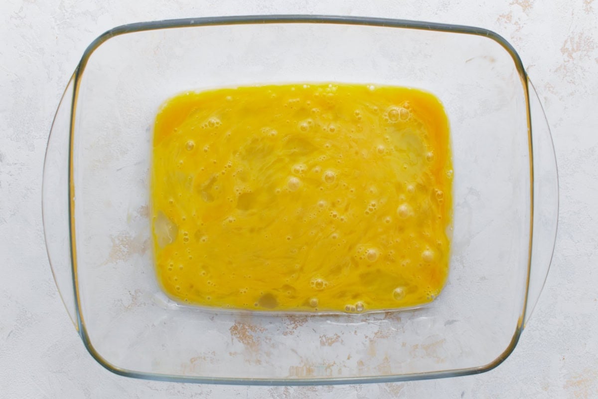 Whisked eggs in a glass dish, ready for dredging chicken in the gluten-free breading process.
