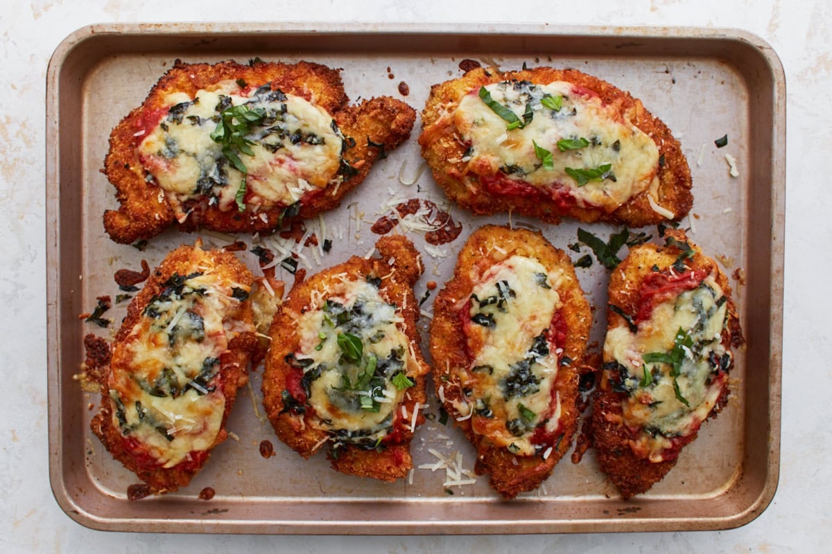 Freshly baked gluten-free chicken parmesan on a sheet pan with melted cheese, bubbly marinara, and garnished with basil.