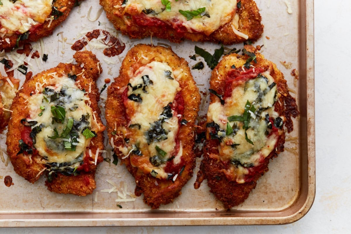 Close-up of golden, baked gluten-free chicken parmesan showing melty cheese, tomato sauce, and crispy edges on a baking tray.