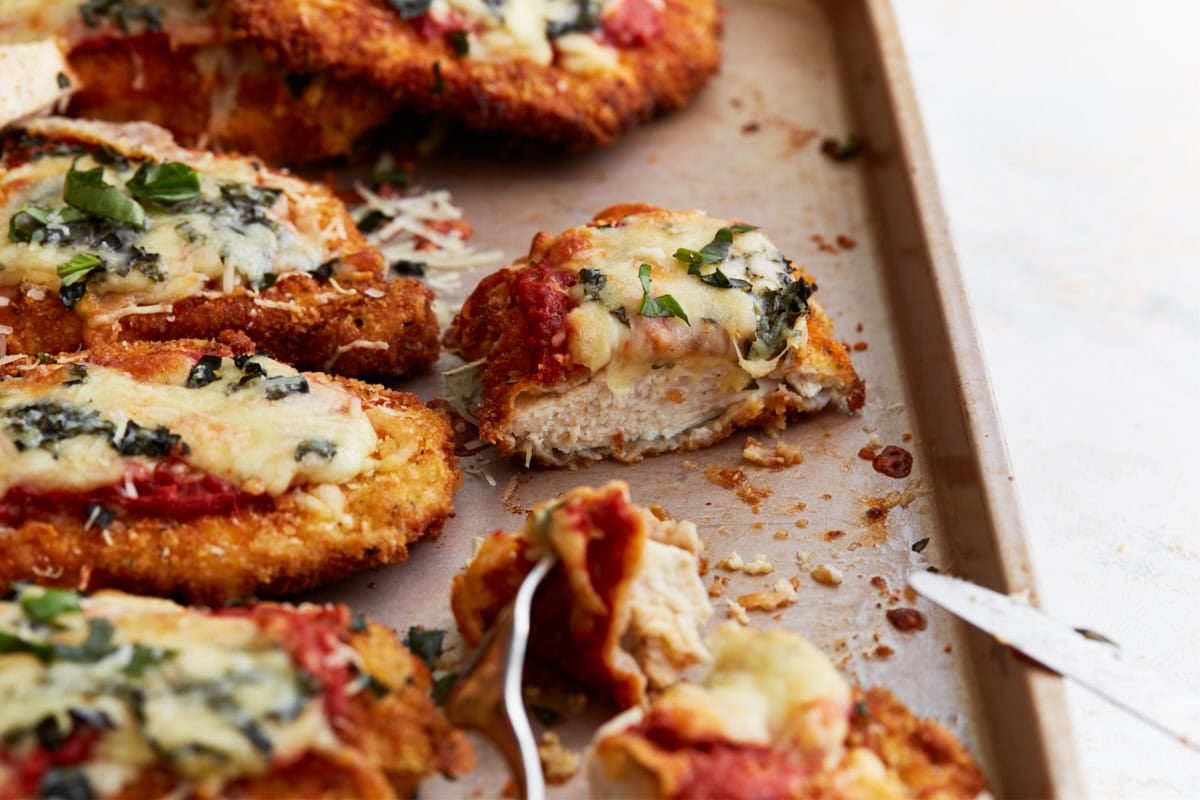 Sliced piece of gluten-free chicken parmesan showing juicy interior with crispy breading, topped with melted cheese and fresh herbs.