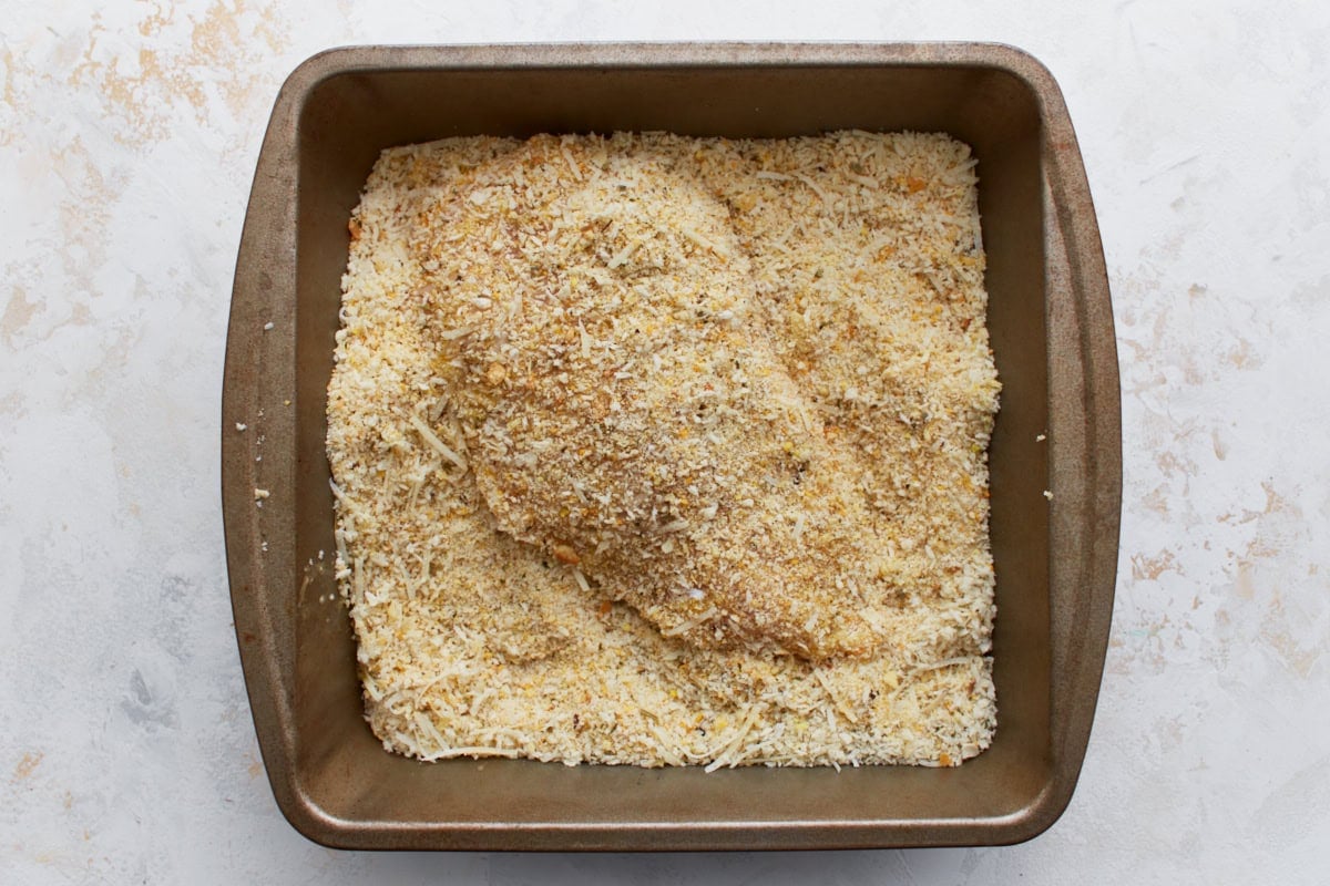 Chicken breast coated in a gluten-free breadcrumb and Parmesan mixture, ready to be cooked.