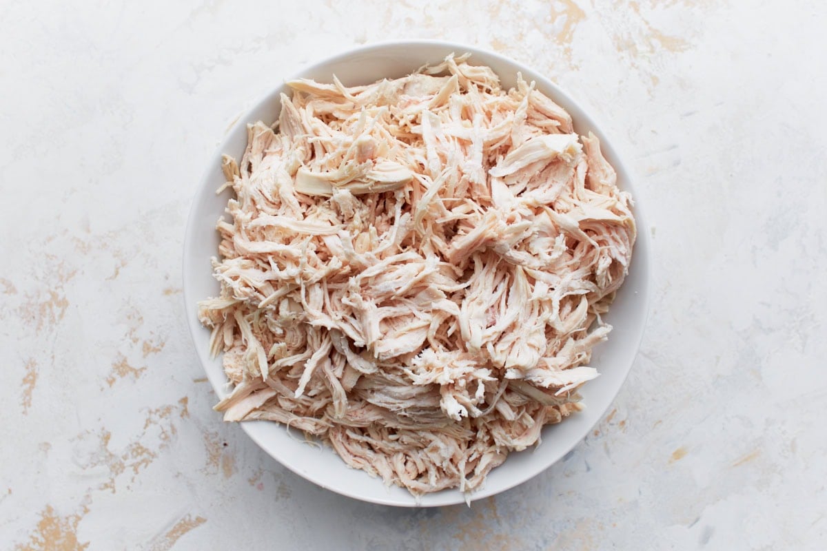 A bowl filled with freshly shredded cooked chicken, ready to be used in the casserole.