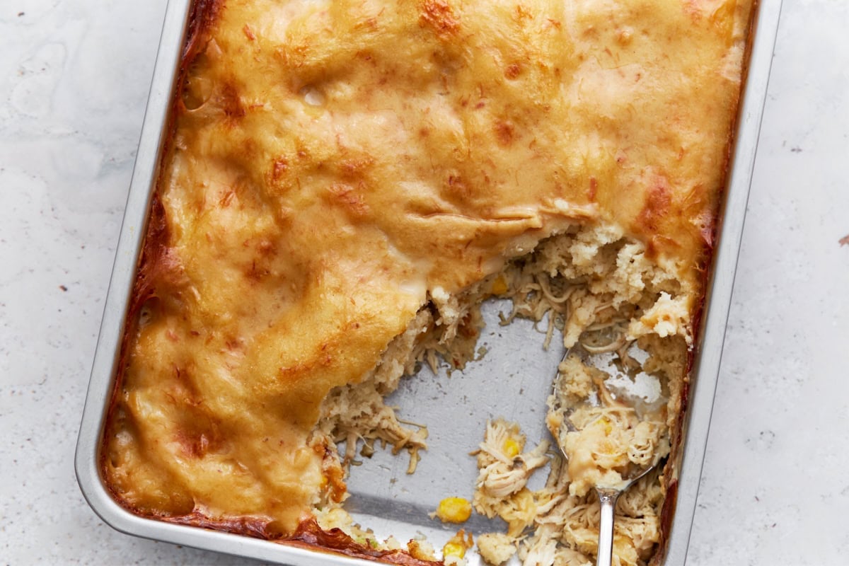 Baking dish with a corner of the casserole scooped out, showing fluffy dumpling layers and creamy shredded chicken underneath.