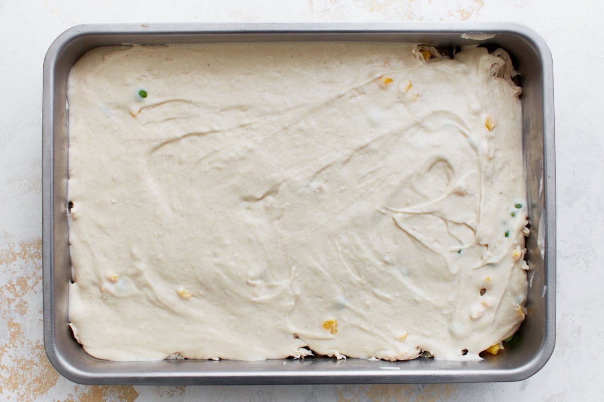 The Bisquick batter layer spread evenly over the chicken and vegetable layer in a baking dish.