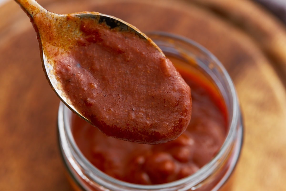 Close-up of a spoonful of thick, smooth enchilada sauce held over the jar.